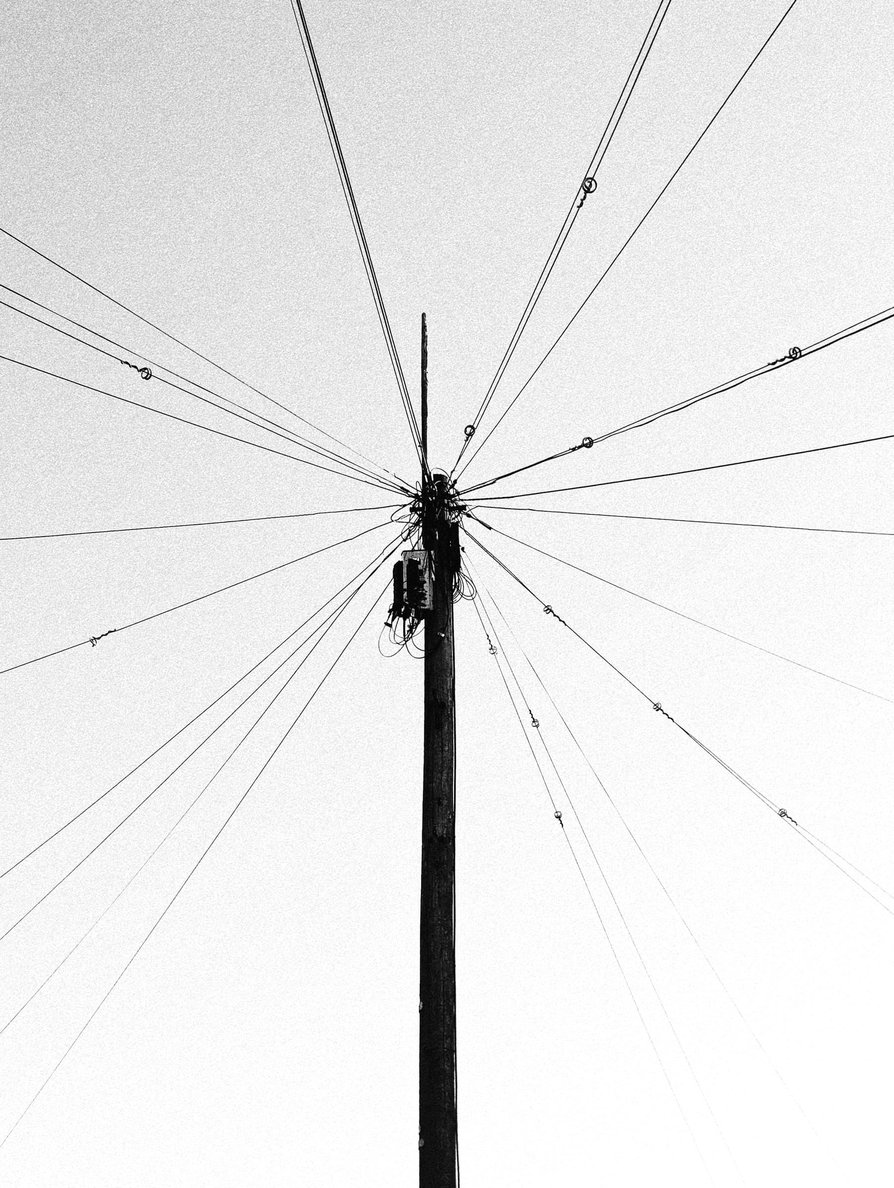 A telephone pole with wires radiating in every direction against a pale sky